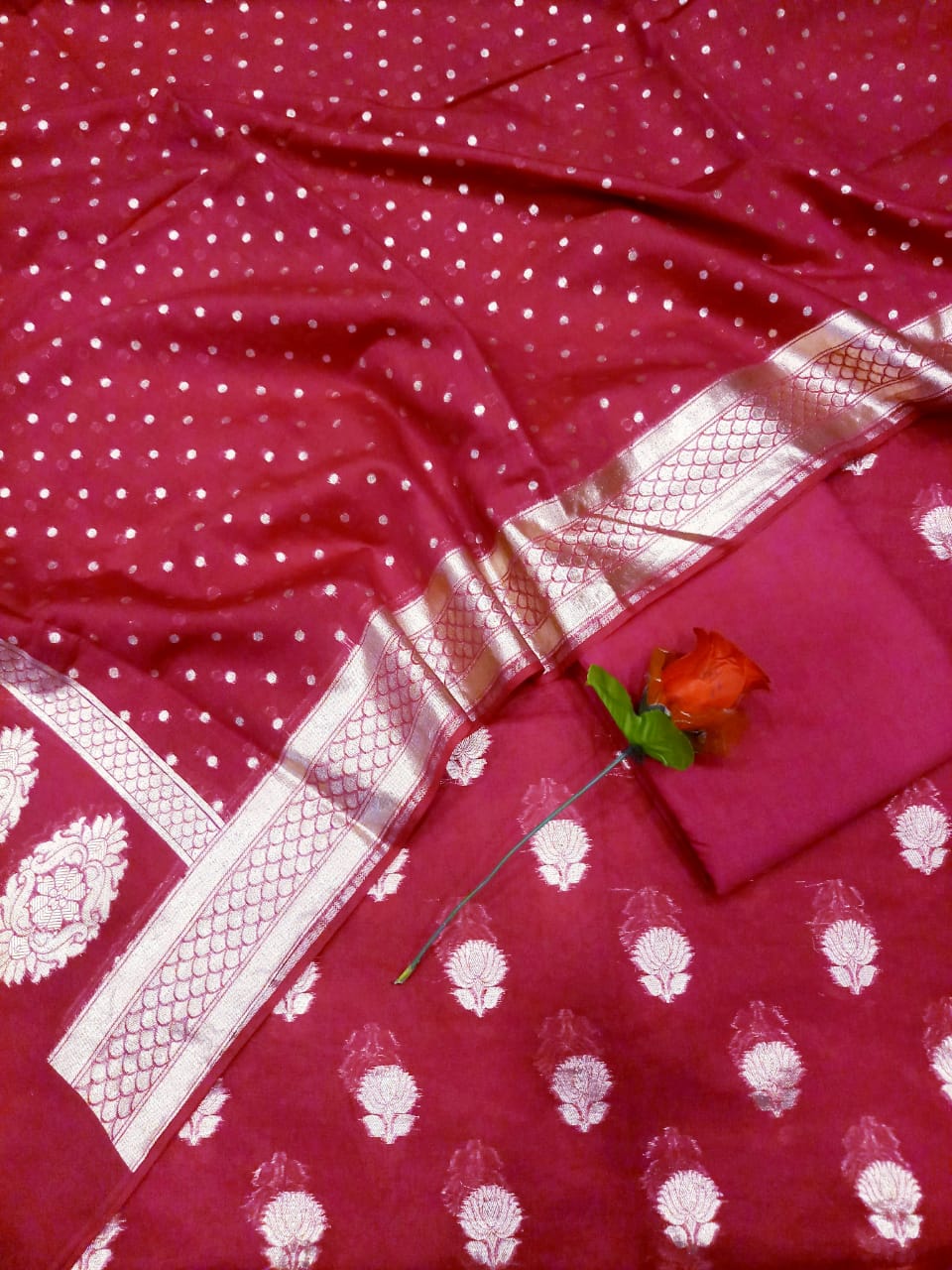 Red fabric with white patterns and a decorative border, featuring a small red flower.