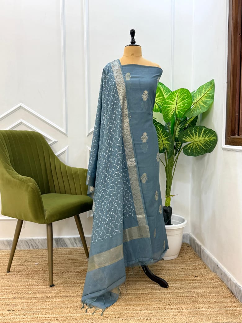 Blue saree with white patterns on a mannequin against a white wall with a green chair and plant.