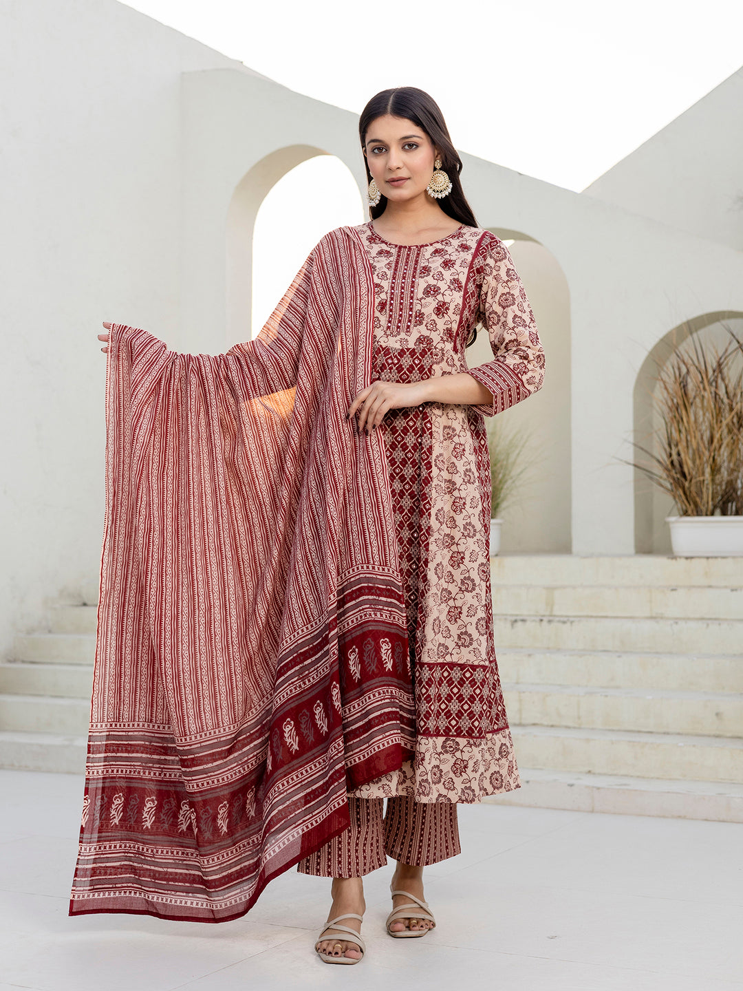 Woman wearing a traditional outfit with a patterned dress and dupatta in a minimalistic setting.