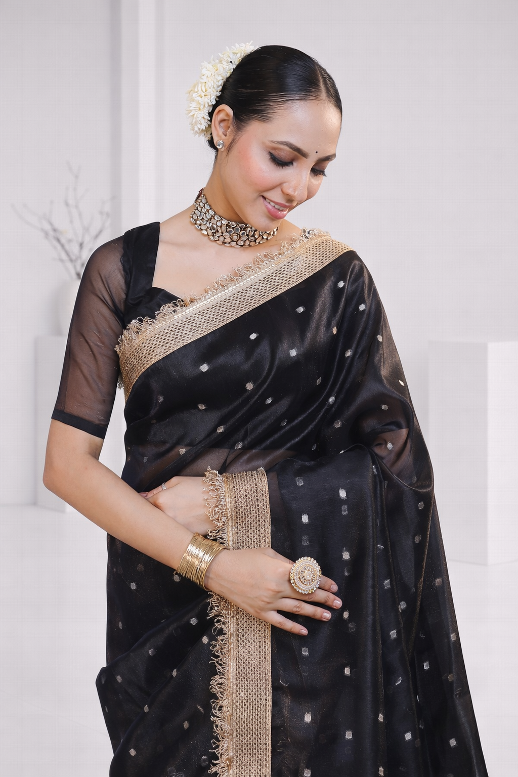Woman wearing a black saree with gold border against a white background