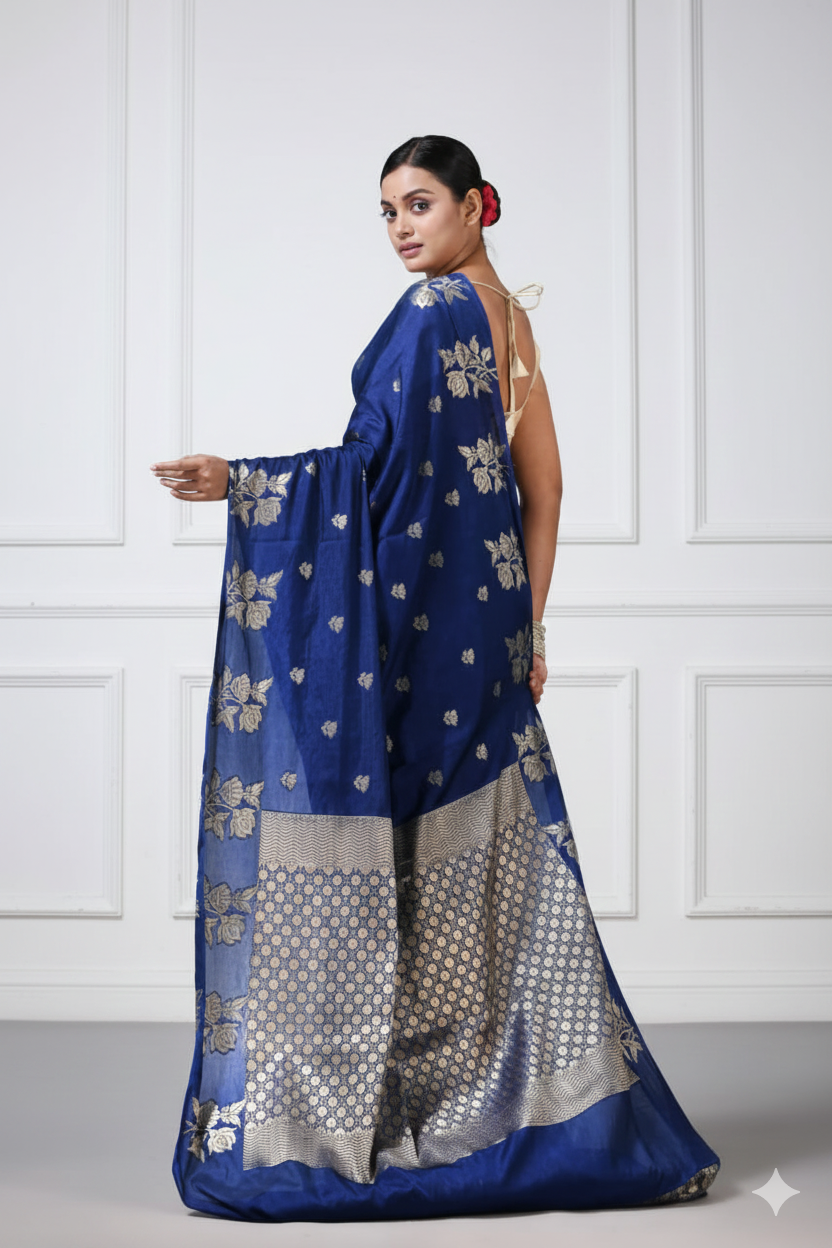 Woman wearing a blue saree with silver patterns against a white paneled wall.