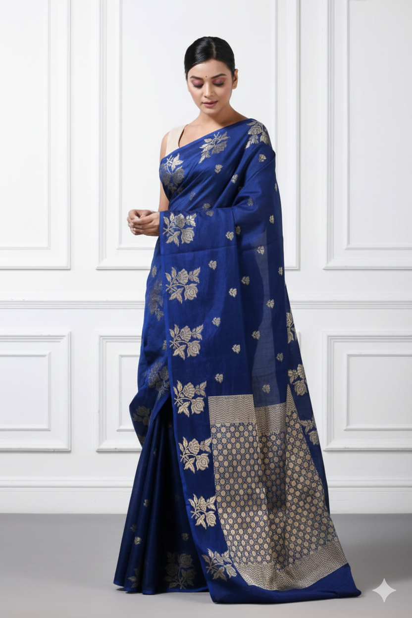 Woman wearing a blue saree with white floral patterns against a white paneled wall.