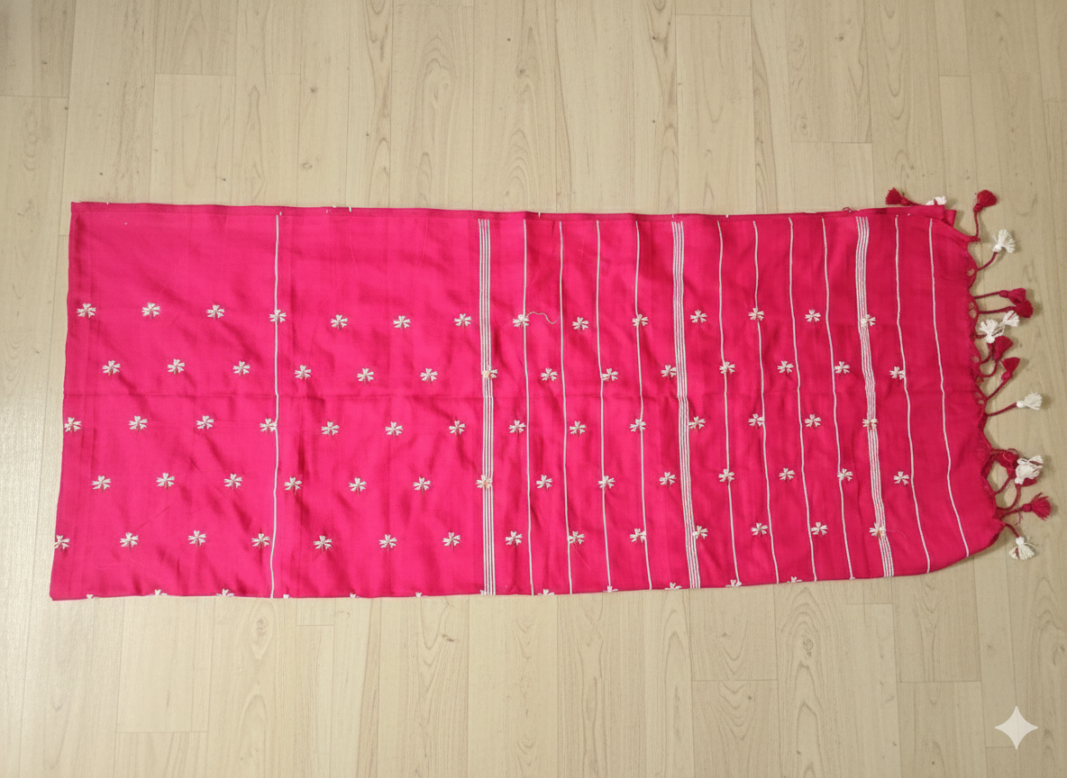 Pink fabric with white floral patterns and red tassels on a wooden surface