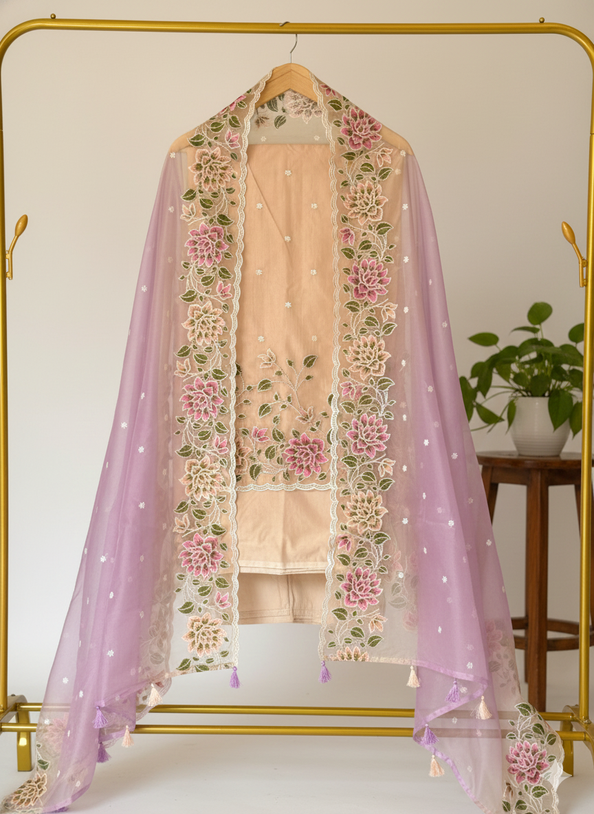 Beige outfit with floral embroidery and pink dupatta on a gold hanger against a white background