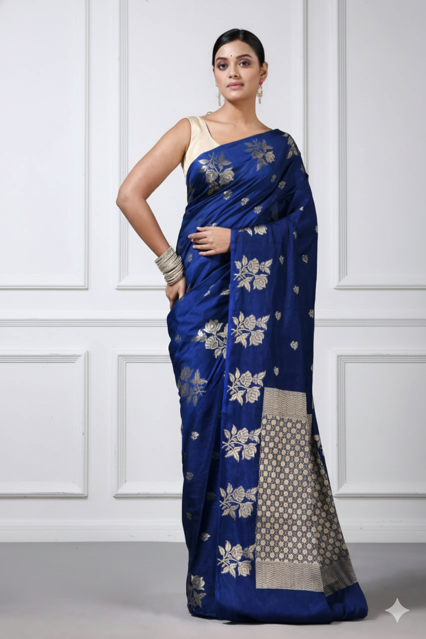 Woman wearing a blue saree with silver patterns against a white paneled wall.