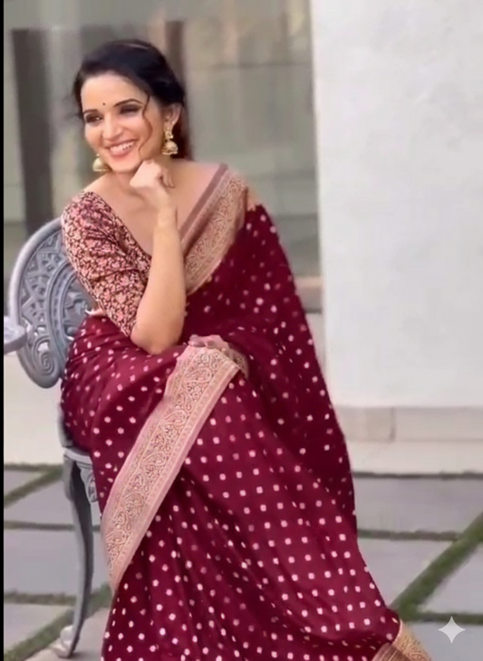 Woman wearing a maroon saree with white patterns, sitting outdoors.