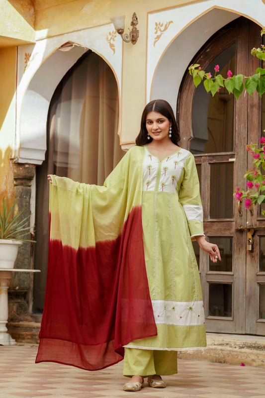 Woman in a green and red traditional outfit standing in front of an architectural background.