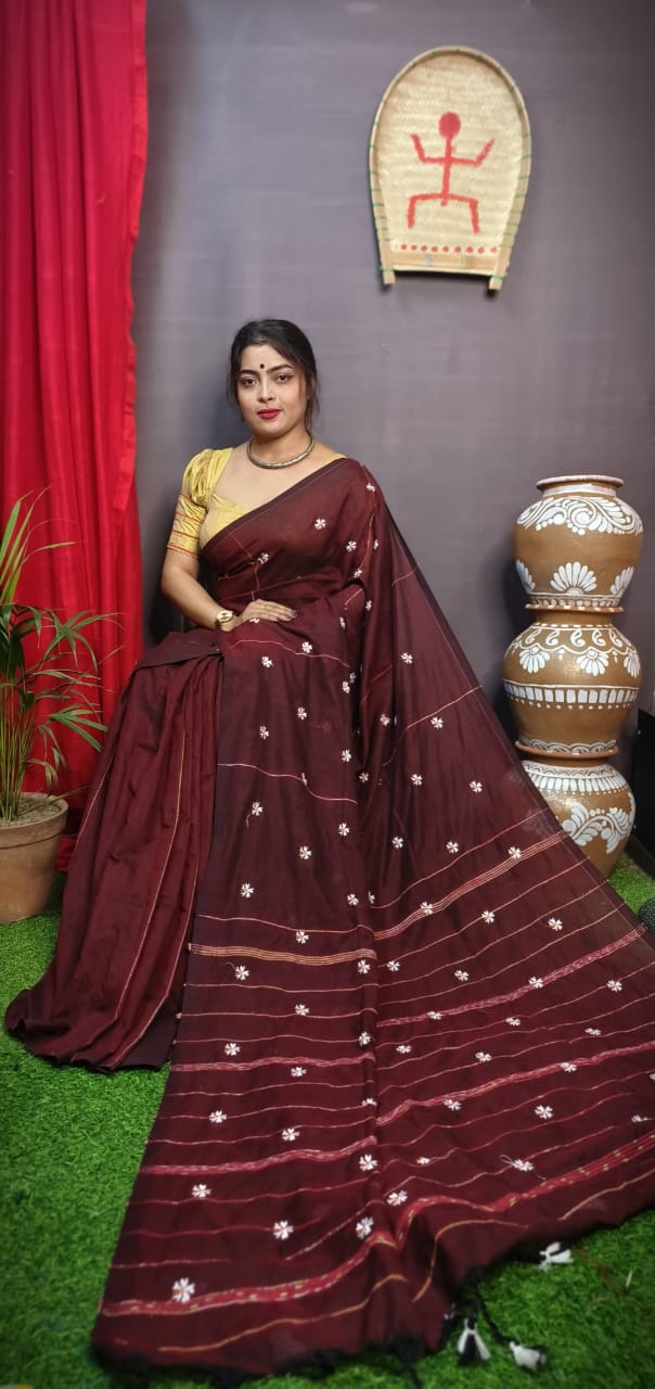 Woman in a maroon saree with white patterns standing against a dark wall with decorative elements.