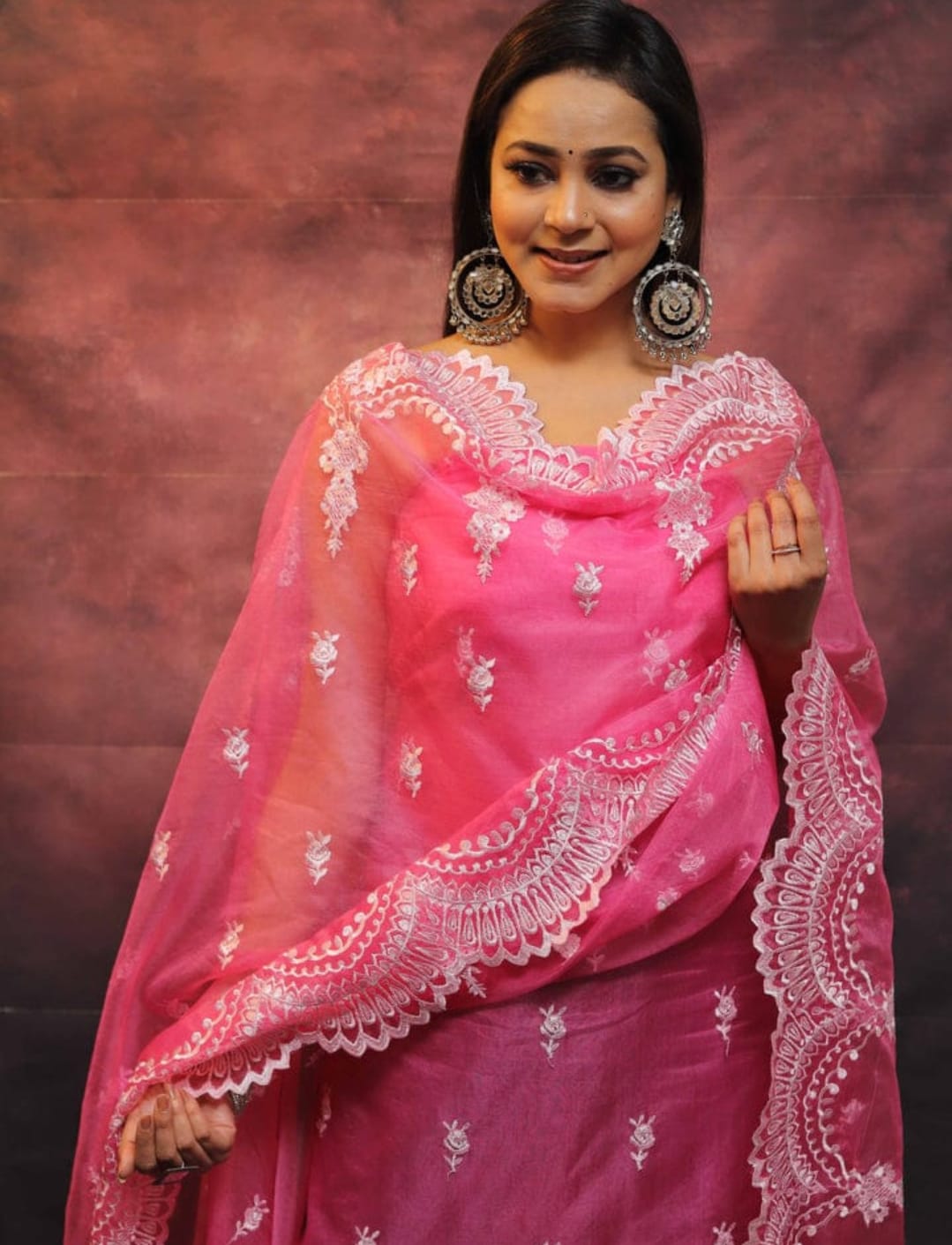 Woman wearing a pink saree with white embroidery against a brown background