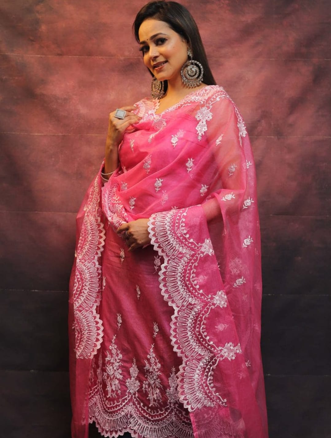 Woman wearing a pink saree with white embroidery against a dark background