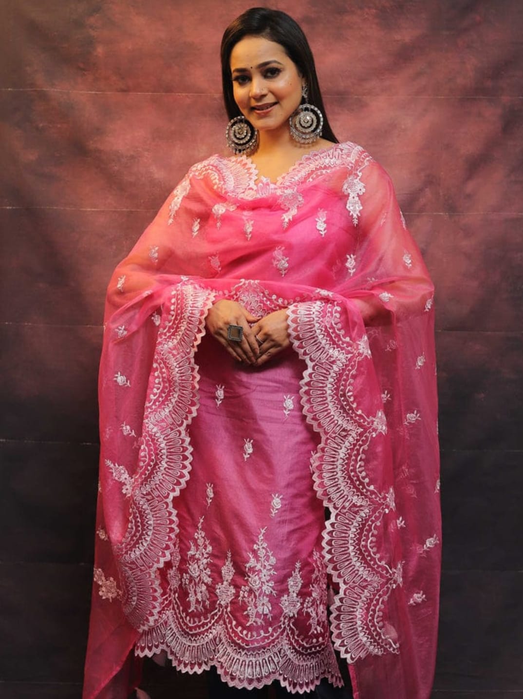 Woman wearing a pink saree with white embroidery against a dark background
