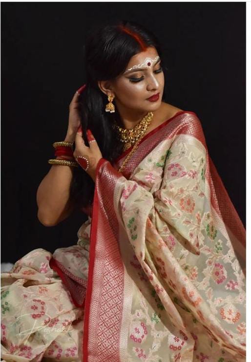 Woman in a traditional saree with floral patterns and red border against a black background
