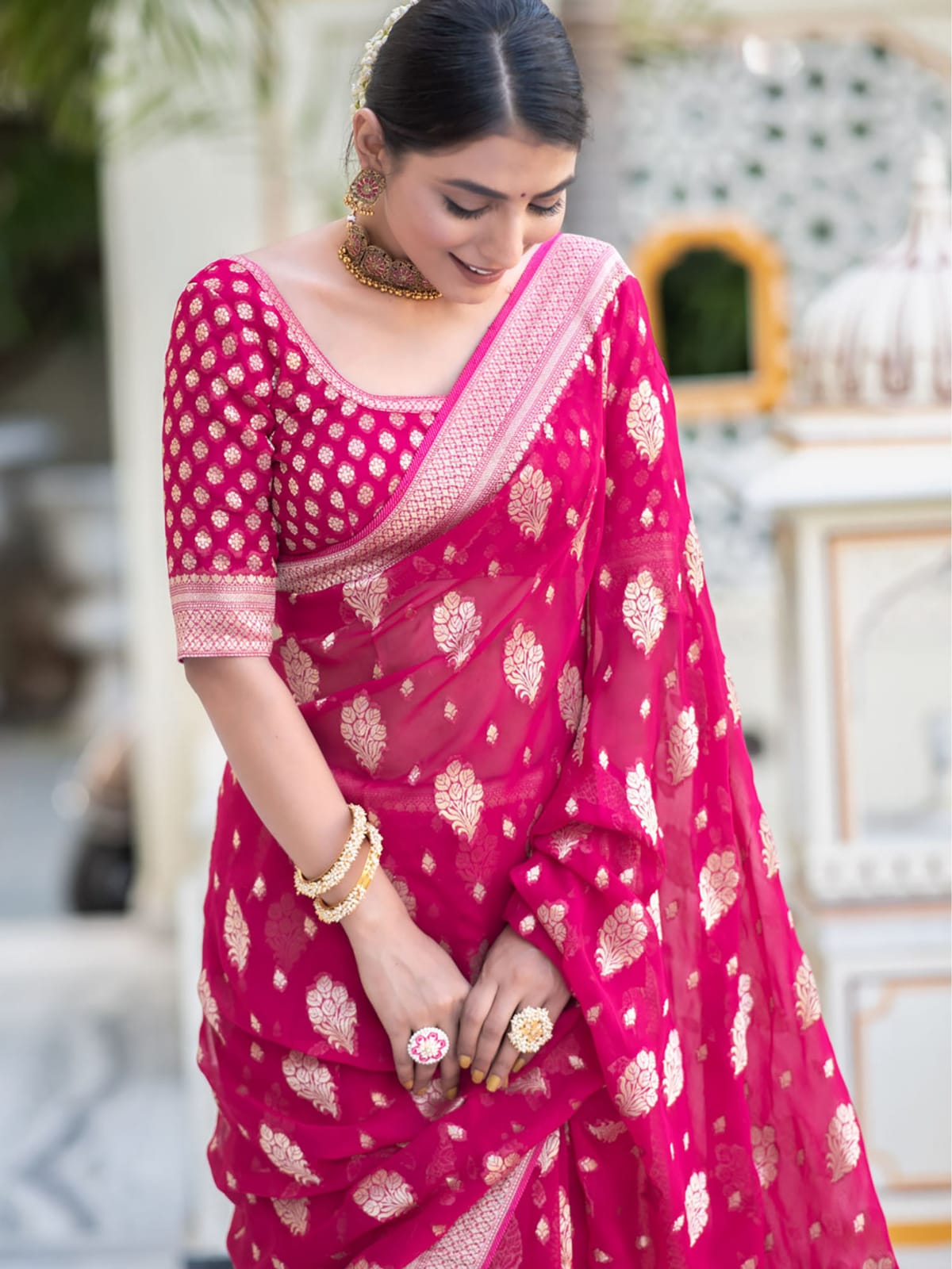 Woman wearing a pink saree with white patterns in an outdoor setting
