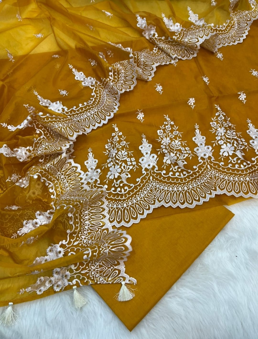 Mustard yellow fabric with intricate white embroidery on a white background