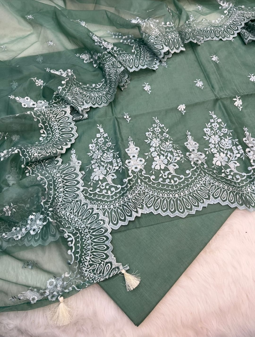 Green fabric with intricate white embroidery and tassels