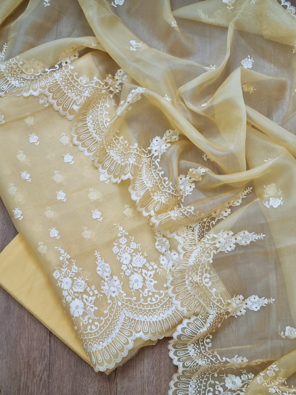 Yellow fabric with white lace embroidery on a wooden surface