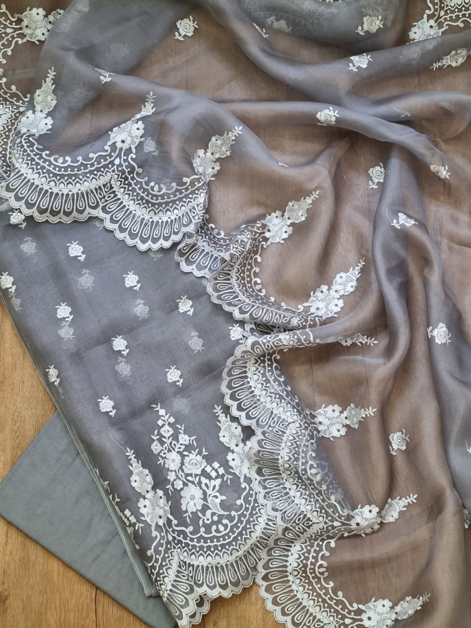 Gray fabric with intricate white lace embroidery on a wooden surface