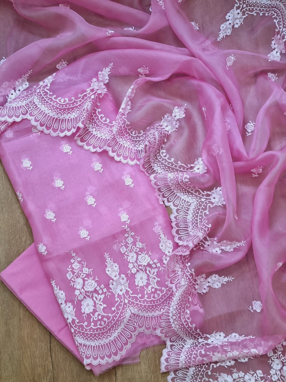 Pink fabric with white lace detailing on a wooden surface