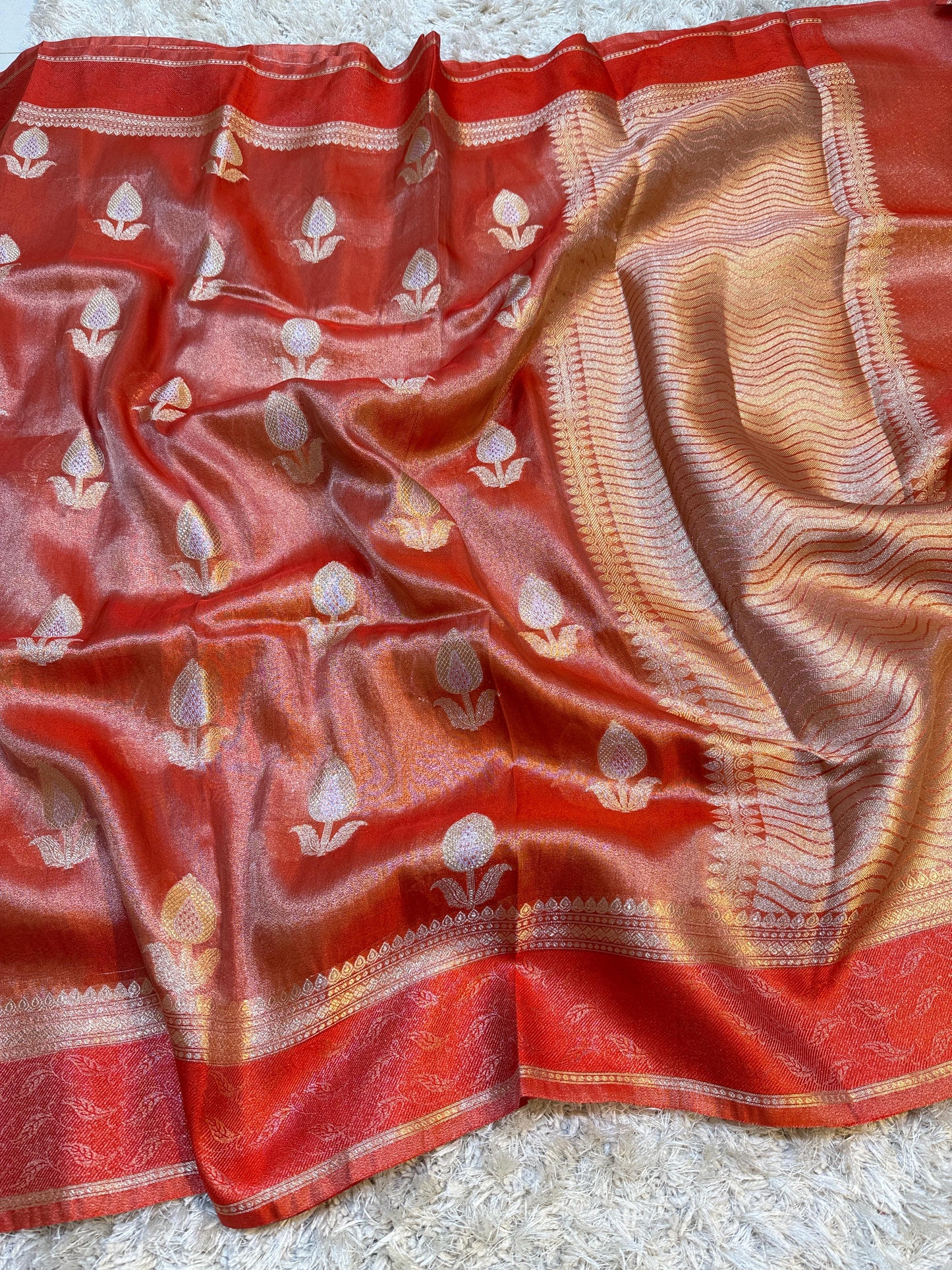Red and gold saree with floral patterns on a textured surface