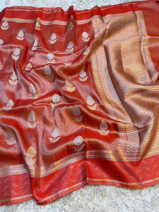 Red and gold saree with floral patterns on a textured surface