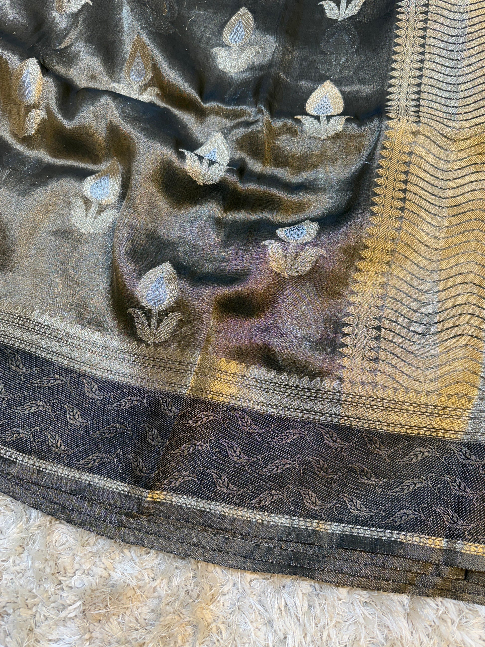 Black saree with gold and white floral patterns on a textured surface