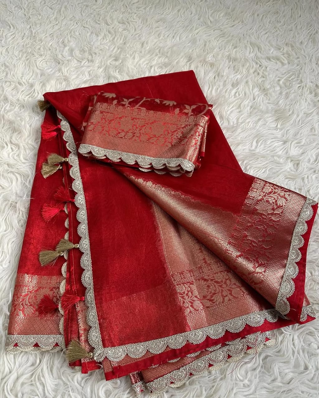 Red saree with silver border and decorative elements on a textured white background