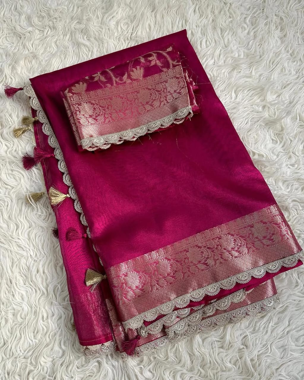 Pink saree with intricate patterns and tassels on a textured white background