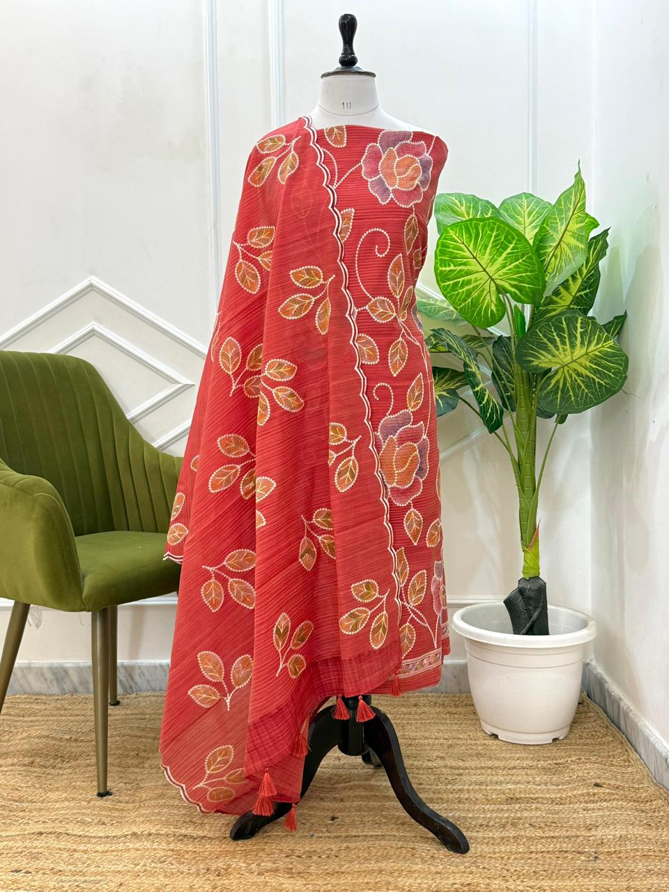 Red floral dress on a mannequin with a green chair and plant in the background