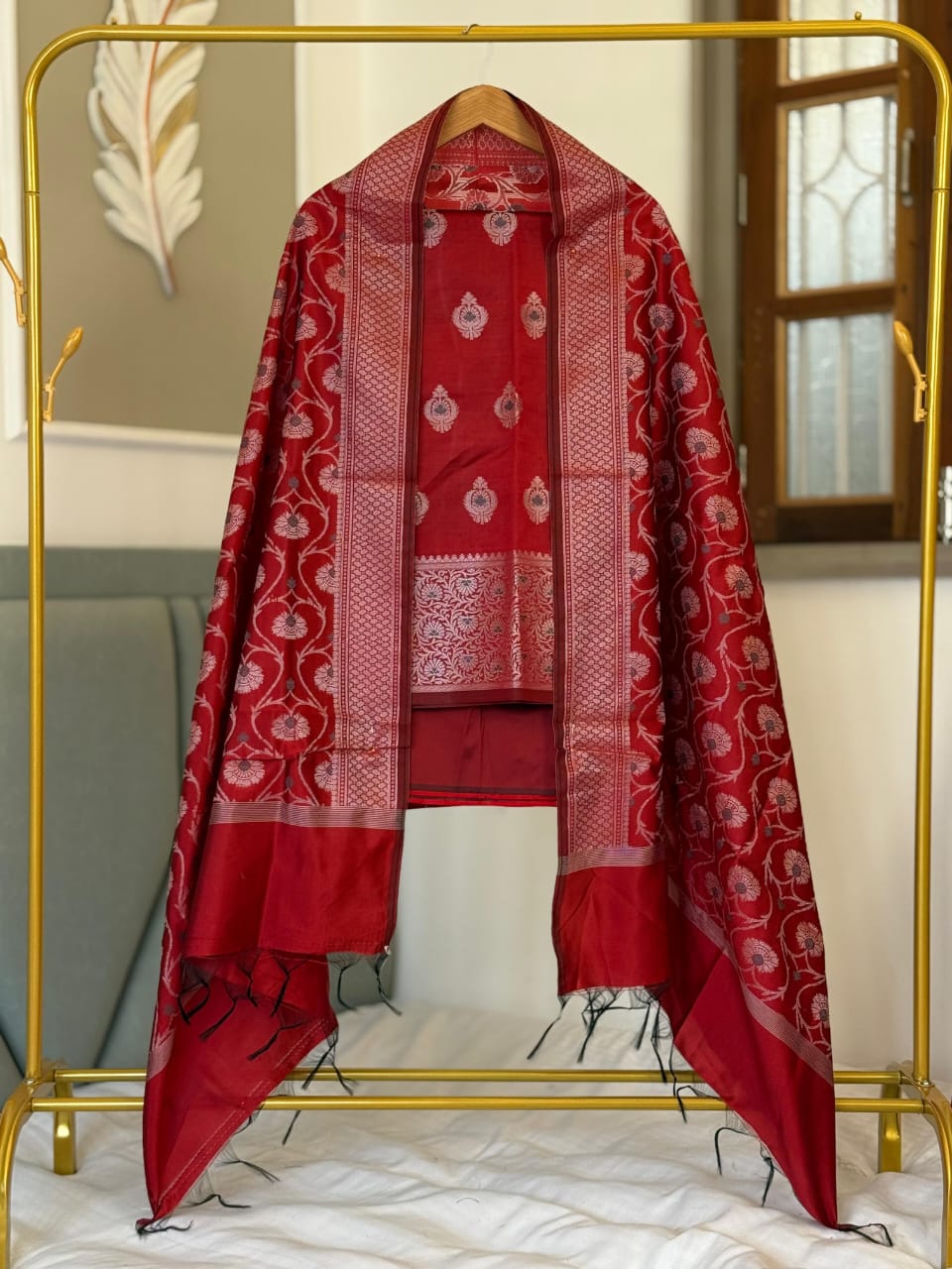 Red traditional outfit with white patterns on a gold stand against a neutral wall.