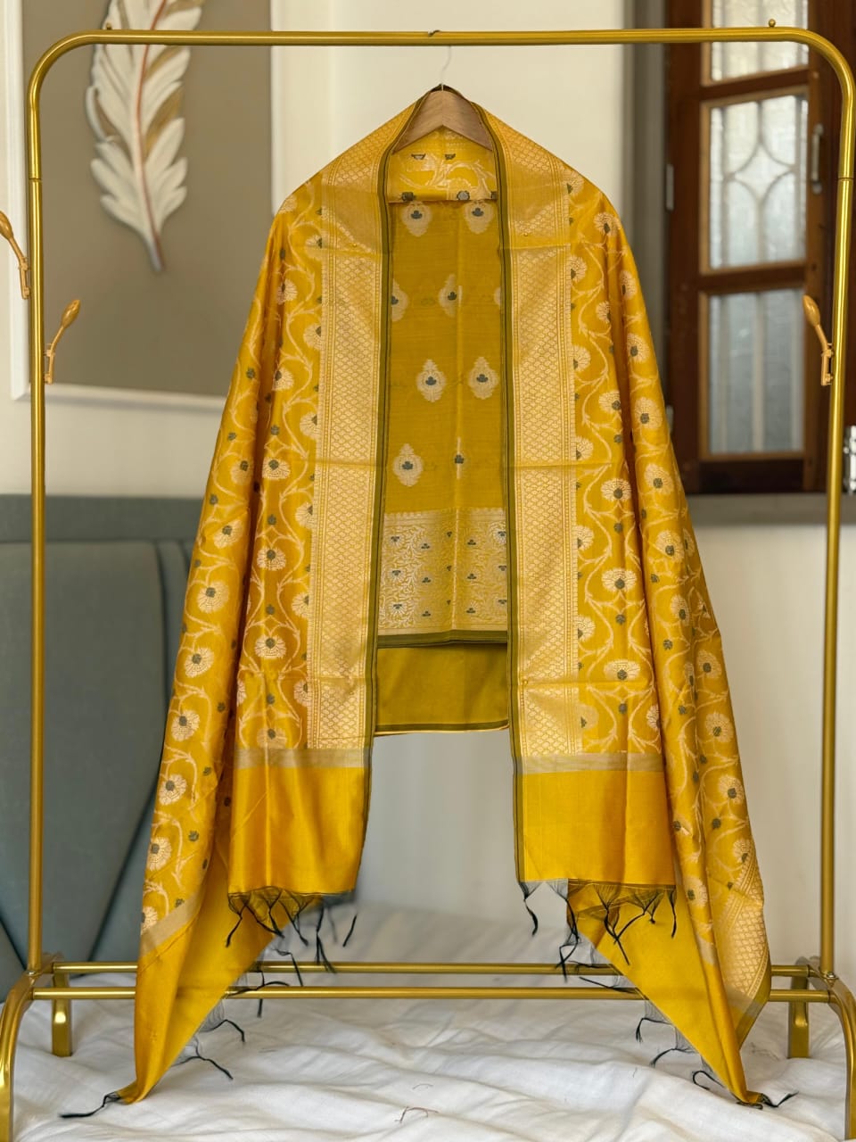 Yellow saree with a gold border draped over a gold stand.