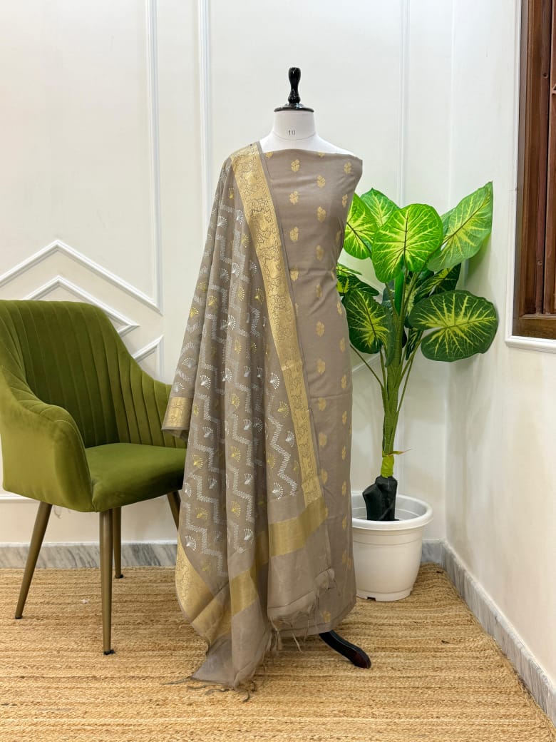 Mannequin wearing a brown saree with gold patterns in a room with a green chair and plant.