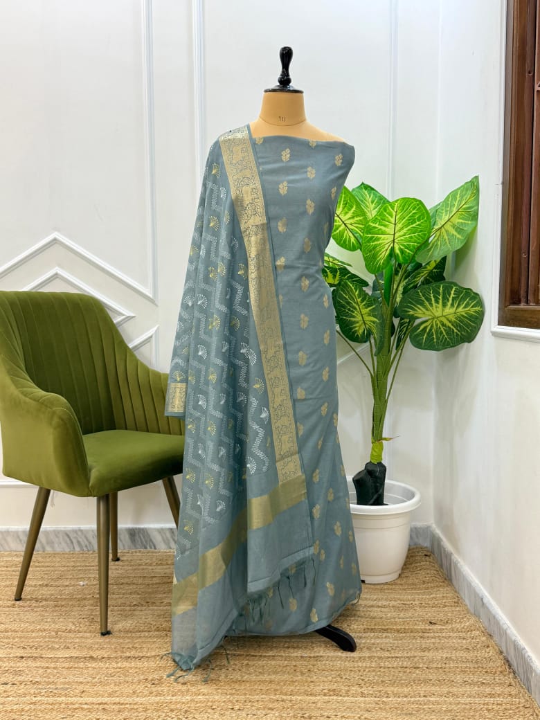 Mannequin wearing a blue saree with gold patterns in a room with a green chair and plant.