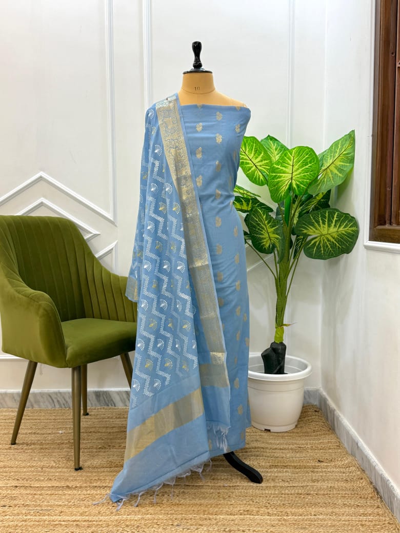 Blue saree with white patterns on a mannequin against a white wall with a plant and chair.