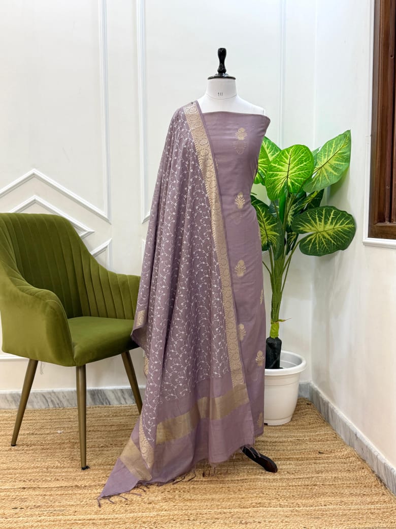 Purple saree with gold border on a mannequin against a white wall with a green chair and plant.