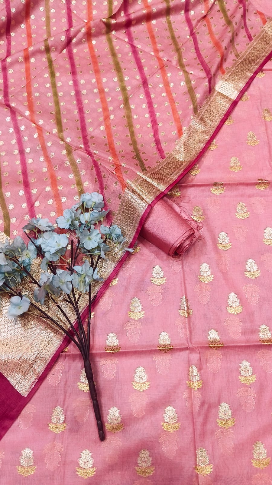 Pink saree with gold patterns and a small bouquet of flowers on a matching pink background