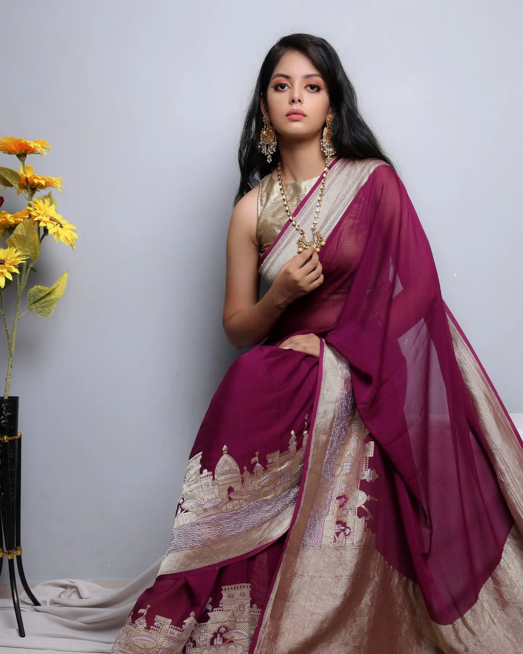 Woman in a purple and gold saree with flowers on a gray background