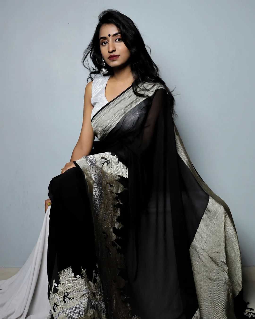 Woman wearing a black and white saree against a plain background