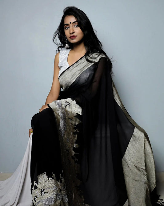 Woman wearing a black and white saree against a plain background