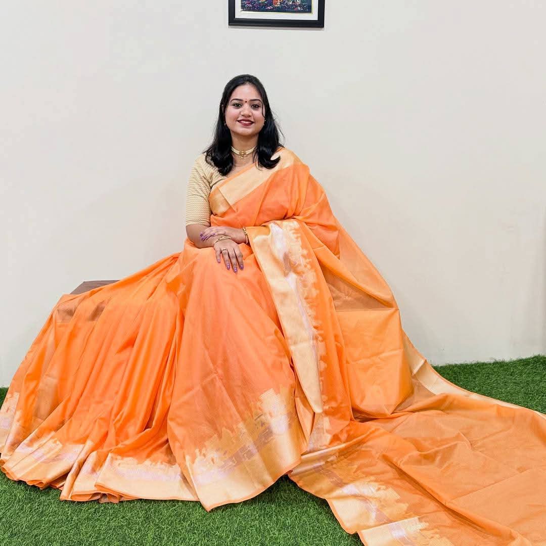 Woman wearing an orange saree sitting on a green surface with a white wall background