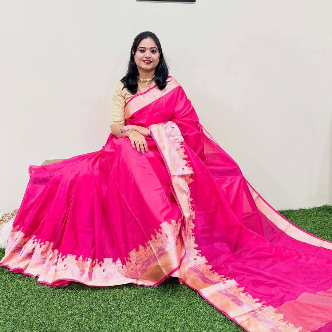 Woman wearing a bright pink saree with a white border on a grassy background