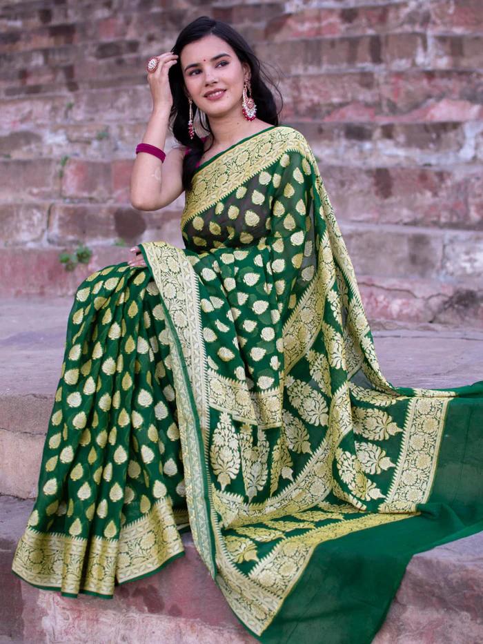 Woman wearing a green saree with gold patterns against a brick wall background