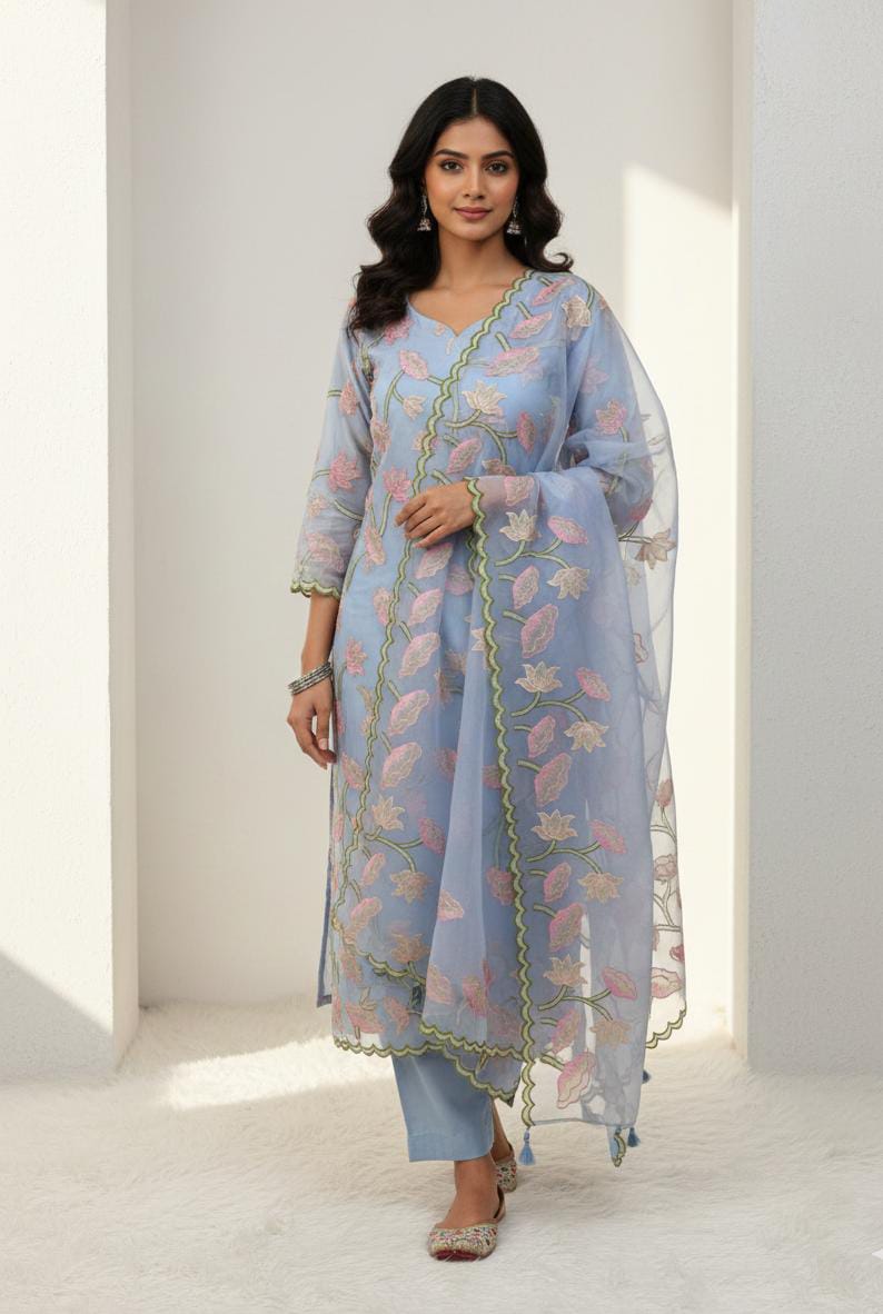 Woman wearing a light blue traditional outfit with floral patterns in a minimalistic setting