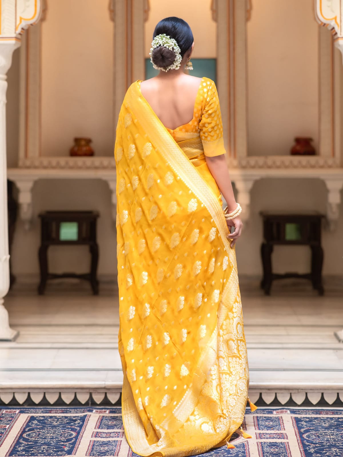 Woman in a yellow saree standing in an ornate indoor setting