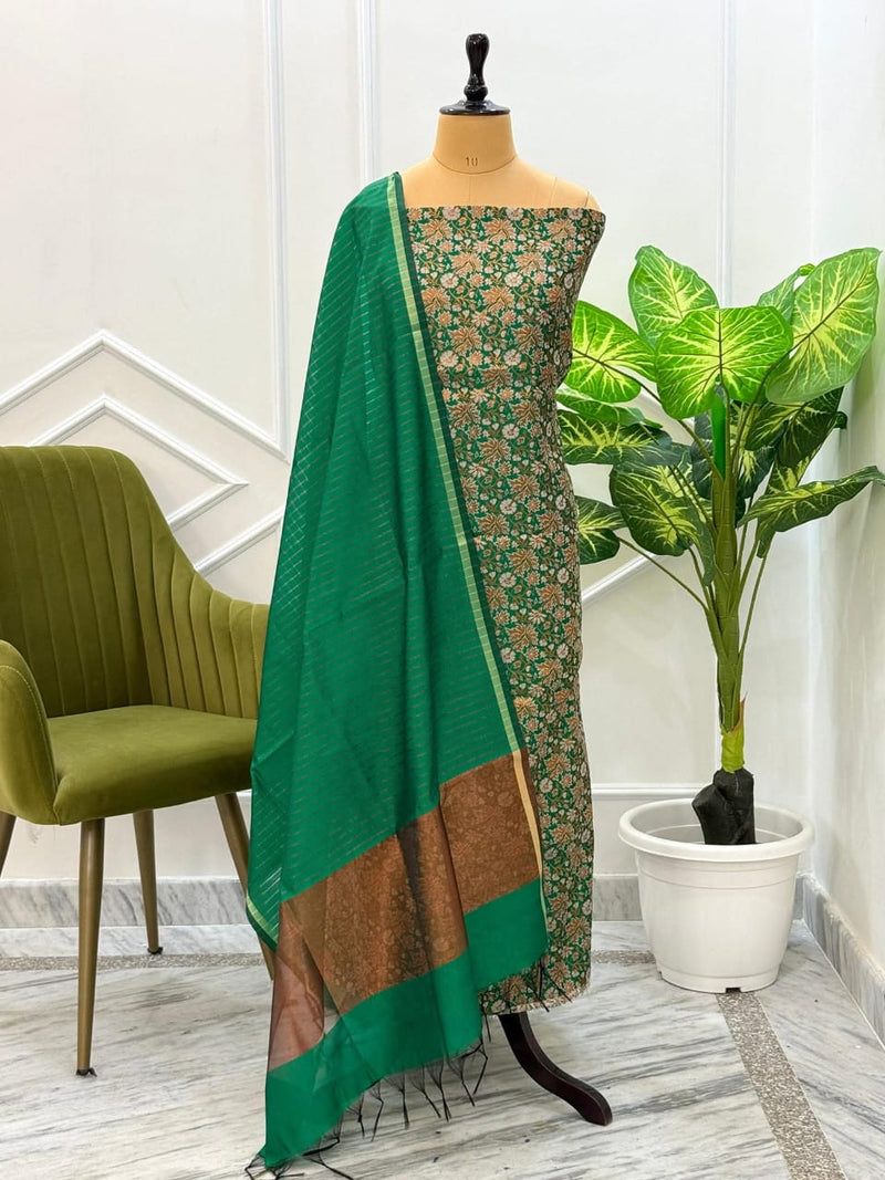 Green saree with floral pattern on a mannequin against a white wall with a plant and chair.