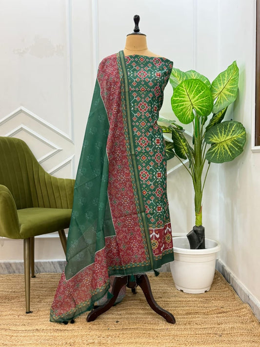 Traditional green and red patterned saree on a mannequin with a plant and chair in the background