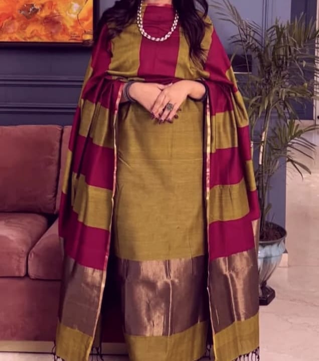 Woman wearing a green and red traditional outfit with a matching shawl in a room.