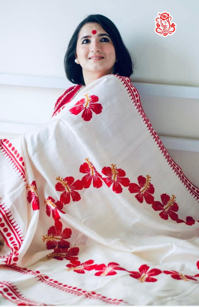 Woman wearing a white saree with red floral embroidery on a plain background