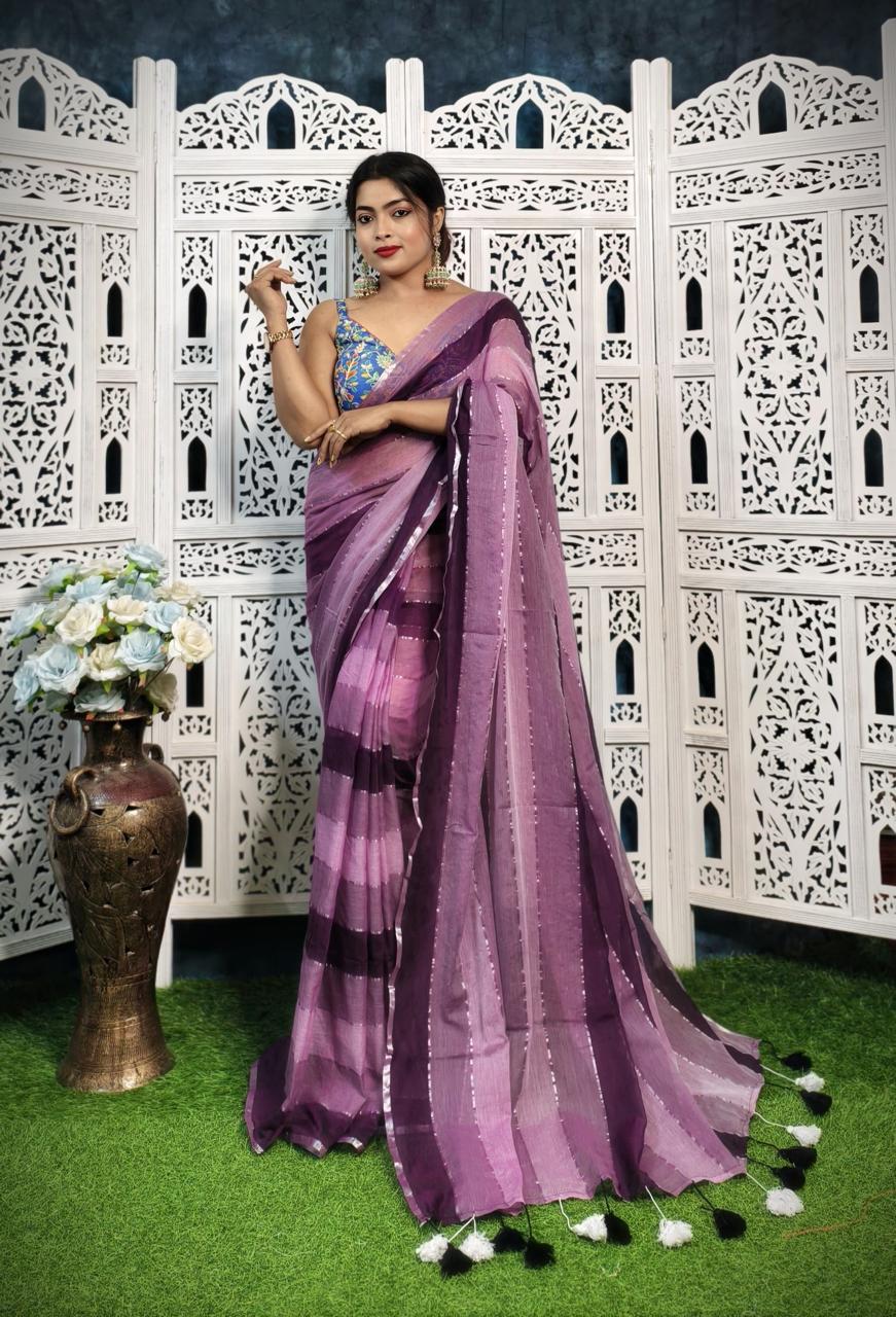 Woman in a purple saree standing in front of a decorative white screen with floral arrangements.
