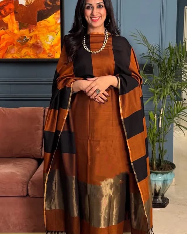 Woman wearing a traditional outfit with a brown and black patterned shawl in a living room setting.