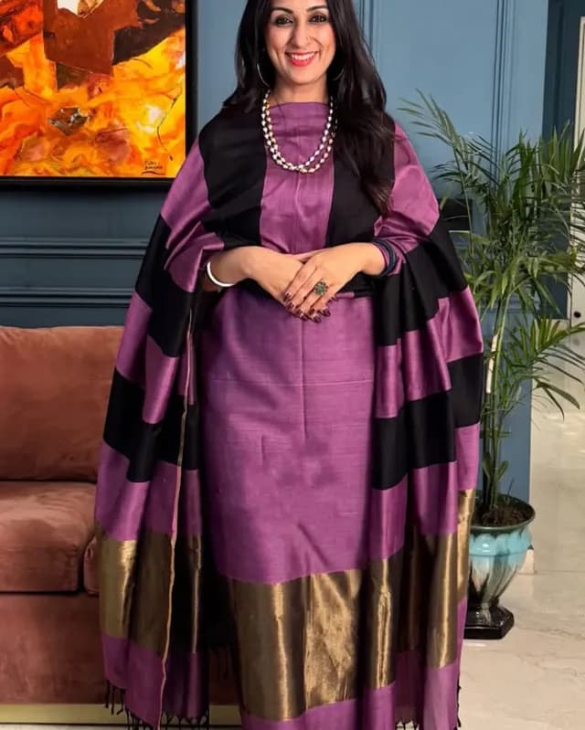 Woman wearing a purple traditional outfit with black and gold accents indoors.